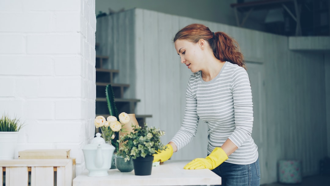 Cheerful young maid is dusting the furniture holding wet cloth in modern light apartment. Housework, people and interiors concept.